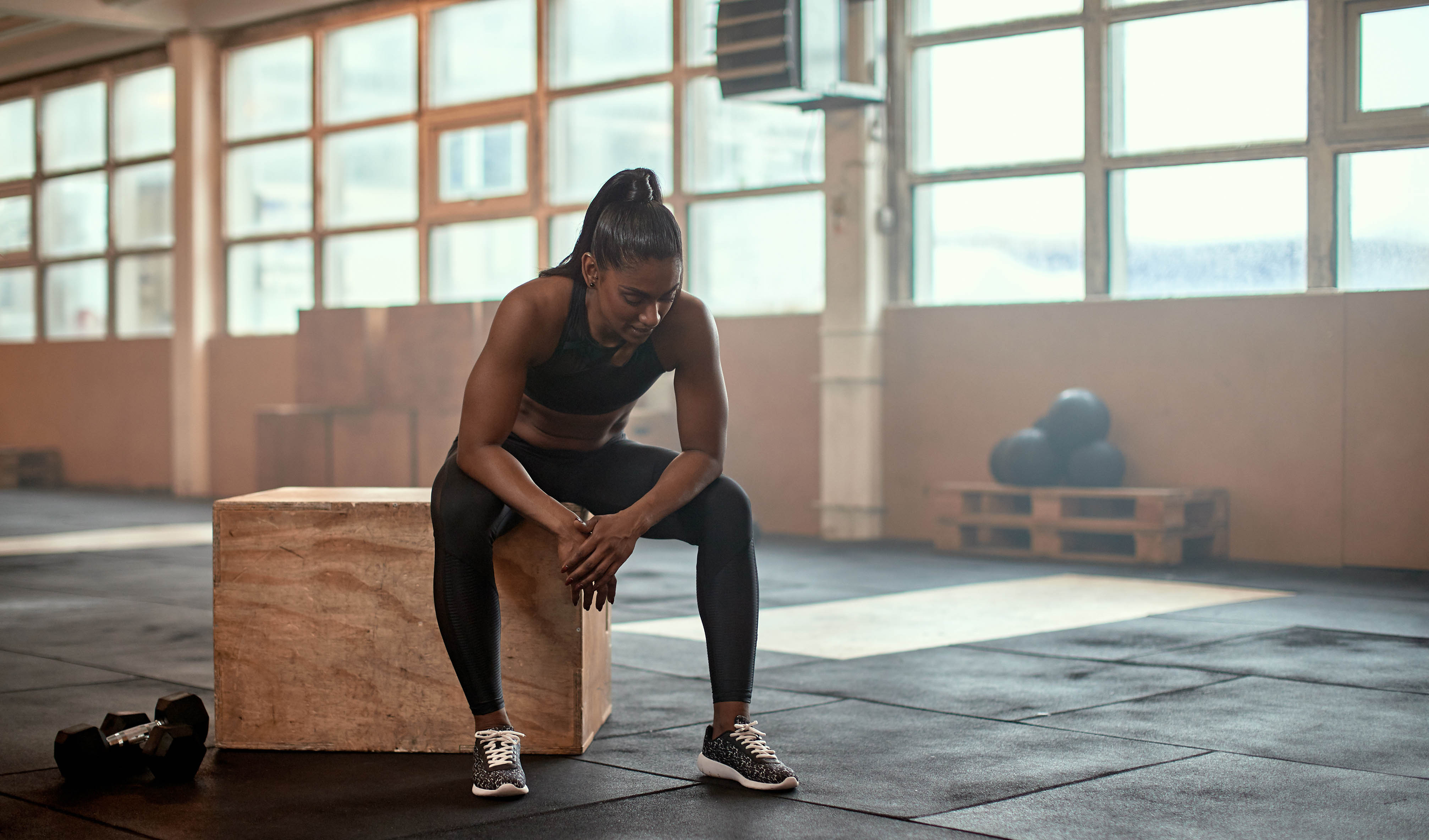 Tired woman sitting on a box, resting for her next set at the gym Tired woman sitting on a box, resting for her next set at the gym